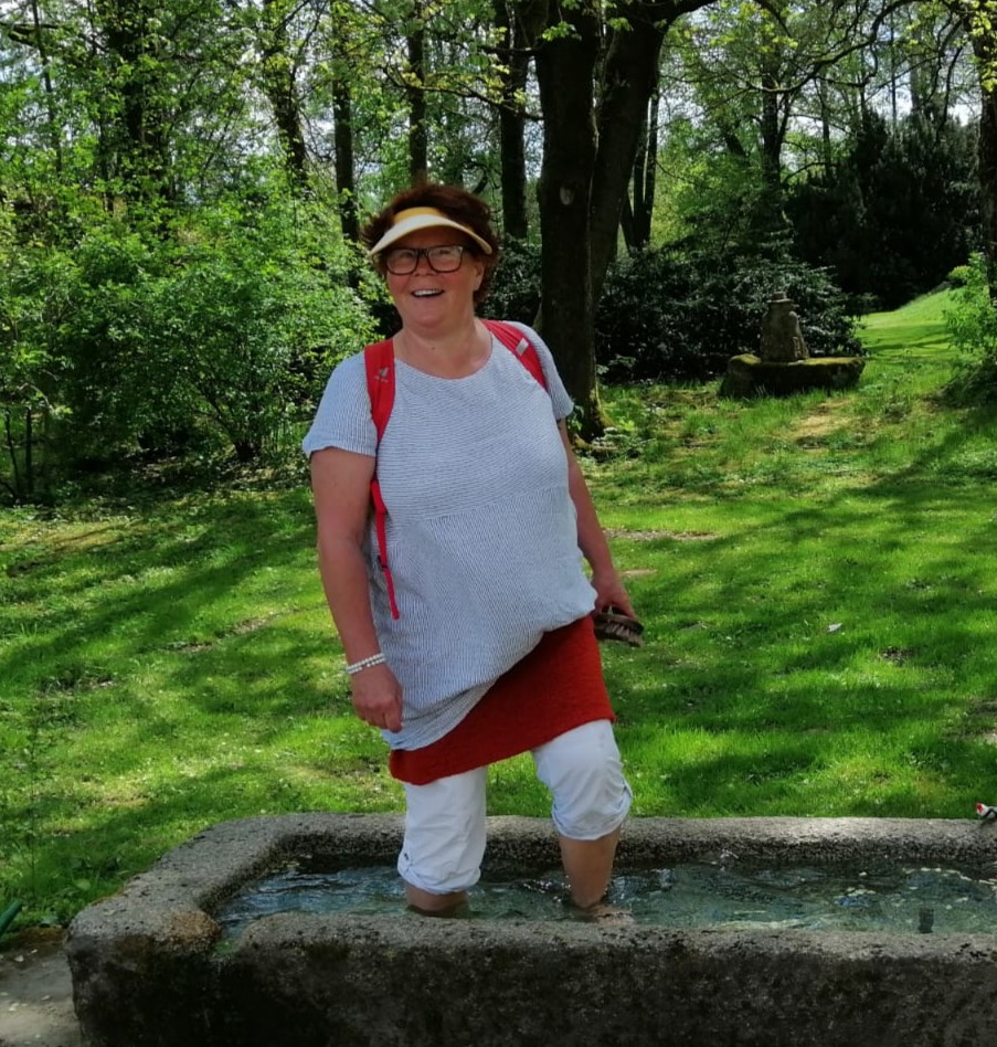 Christine König steht lächelnd mit ihren nackten Füßen im Wasser